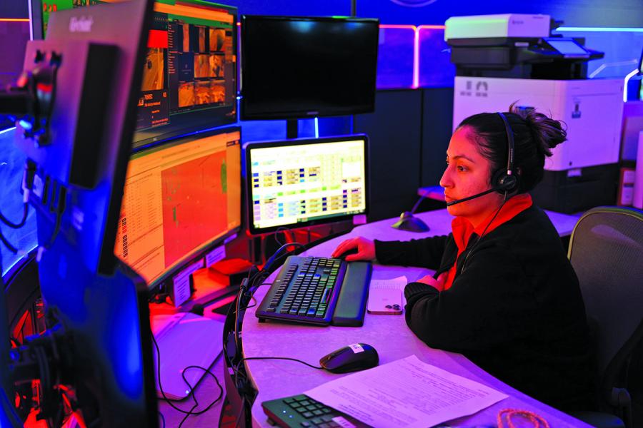 A public safety dispatcher works at a desk with several monitors