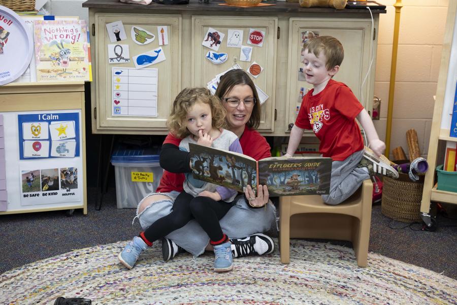 Children gather around an adult reading a story to them